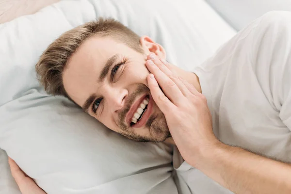 Молодий чоловік лежить у ліжку і страждає від зубного болю — стокове фото
