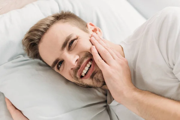 Joven acostado en la cama y sufriendo de dolor de muelas - foto de stock