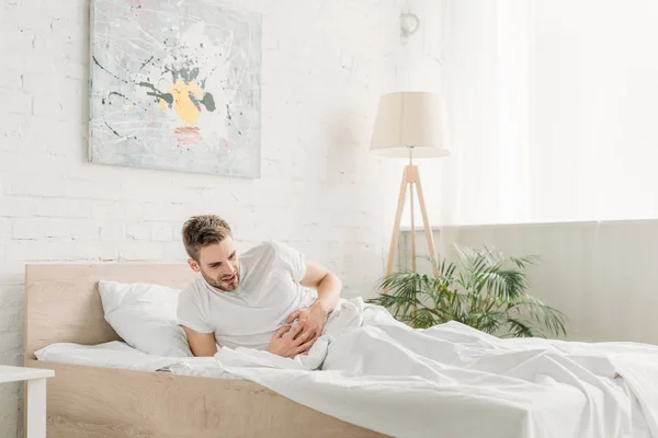 Young man touching stomach while suffering from abdominal pain in bedroom — Stock Photo