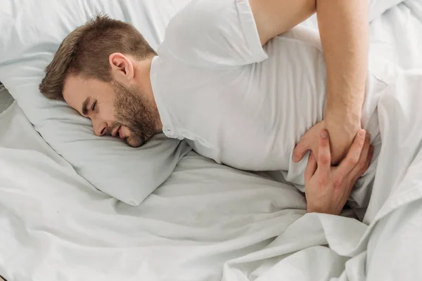 Young man lying in bed and suffering from stomach pain with closed eyes — Stock Photo