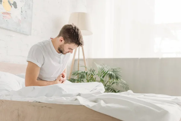Young man sitting in bed and suffering from abdominal pain — Stock Photo