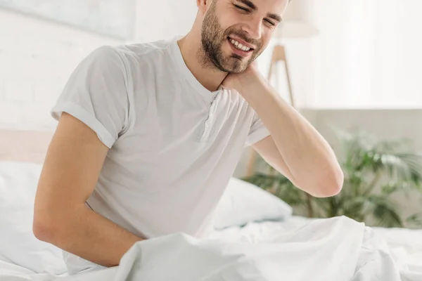 Young man sitting on bed and suffering from neck pain with closed eyes — Stock Photo