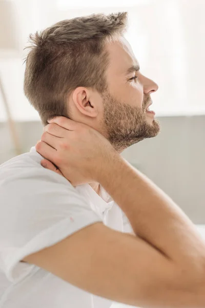 Vista lateral del joven tocando el cuello mientras sufre de dolor con los ojos cerrados - foto de stock