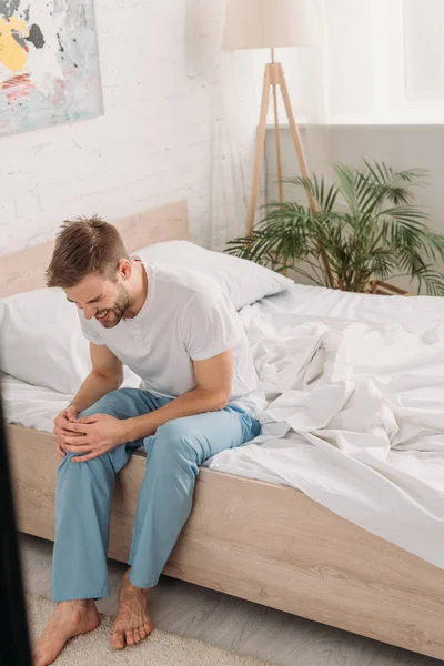 Junger Mann sitzt auf Bett und leidet unter Knieschmerzen — Stockfoto