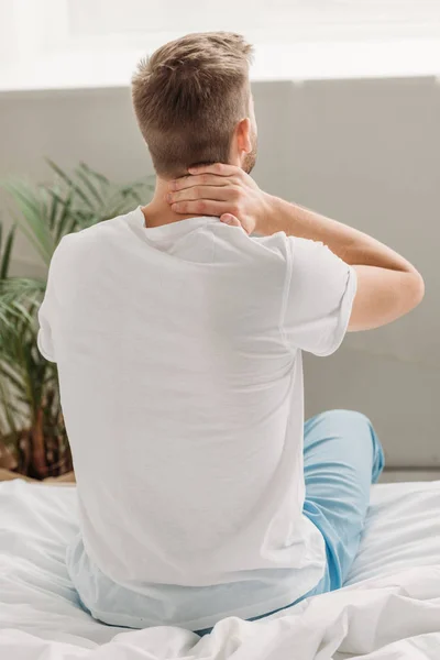 Back view of man sitting on white bedding and suffering from neck pain — Stock Photo