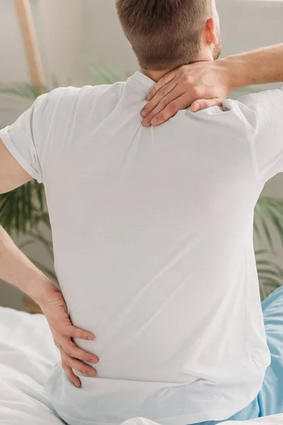 Visão traseira do homem sentado na cama e sofrendo de dor nas costas — Fotografia de Stock