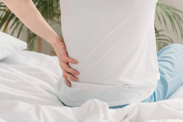 Cropped view of man sitting on bed and suffering from loin pain — Stock Photo