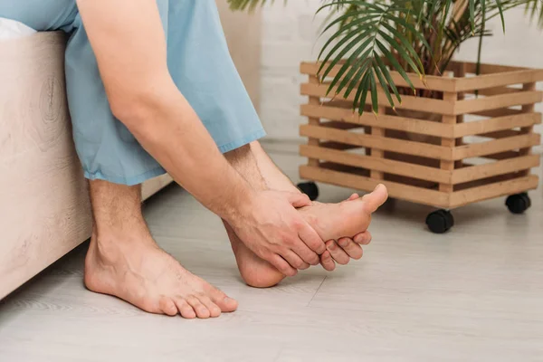 Vue recadrée homme touchant le pied tout en étant assis sur le lit et souffrant de douleur — Photo de stock