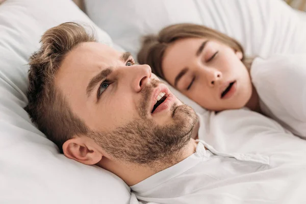 Aufgeweckter Mann schaut auf, während er neben schnarchender Frau im Bett liegt — Stockfoto