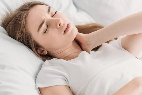 Молодая женщина лежит в постели с закрытыми глазами, страдая от боли в шее — стоковое фото