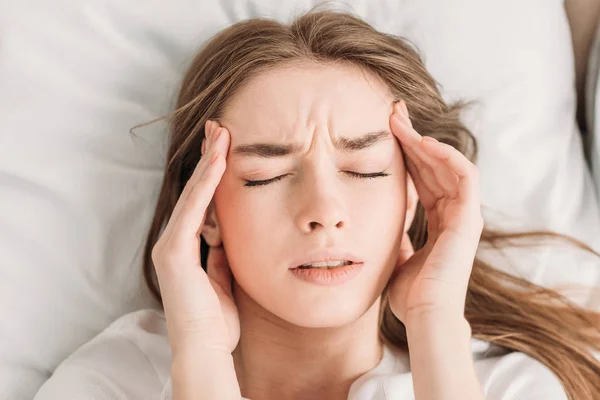 Vista superior de la mujer joven con los ojos cerrados tocando la cabeza mientras sufre de migraña - foto de stock