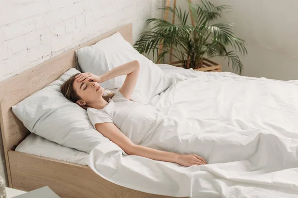 Молодая женщина лежит в постели с закрытыми глазами и страдает от мигрени — стоковое фото