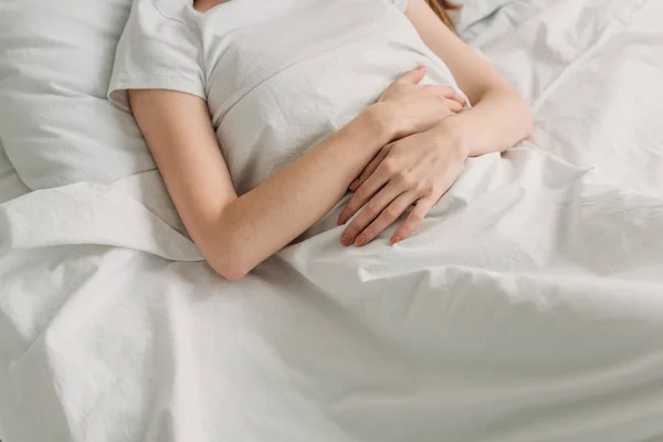 Vista recortada de la mujer acostada en la cama y que sufre de dolor de estómago - foto de stock