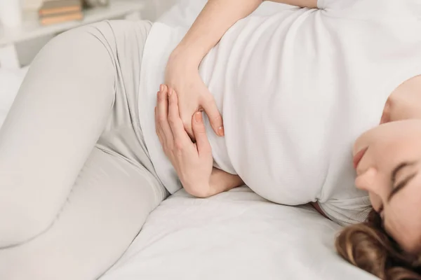 Vista recortada de la niña acostada en la cama y que sufre de dolor de estómago - foto de stock