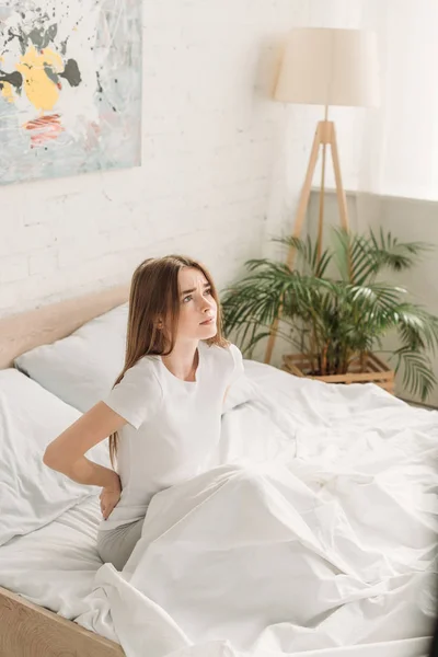 Upset girl looking away while sitting in bed and suffering pram back pain — Stock Photo