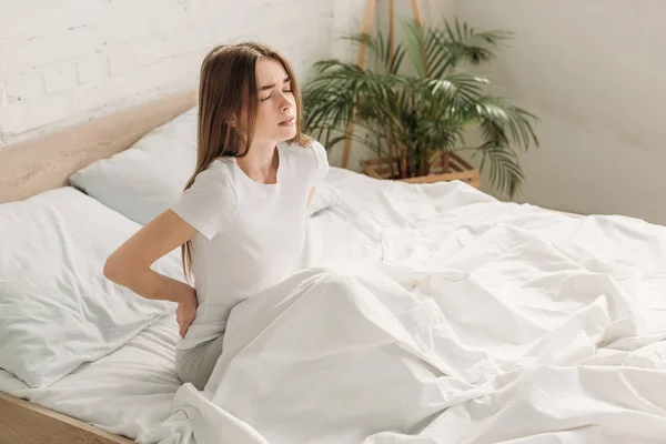 Jeune femme assise au lit et souffrant de douleurs dans la longe — Photo de stock