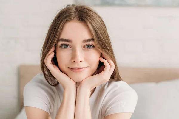 Positive jeune femme souriant à la caméra tout en tenant la main près du visage — Photo de stock