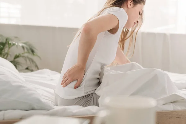 Junge Frau sitzt im Bett und leidet unter Lendenschmerzen — Stockfoto