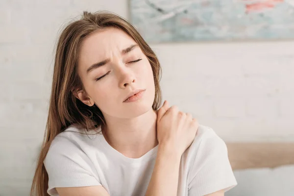 Frowned girl with closed eyes touching neck while suffering from pain — Stock Photo
