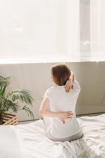 Back view of girl sitting on bed and suffering from back pain — Stock Photo
