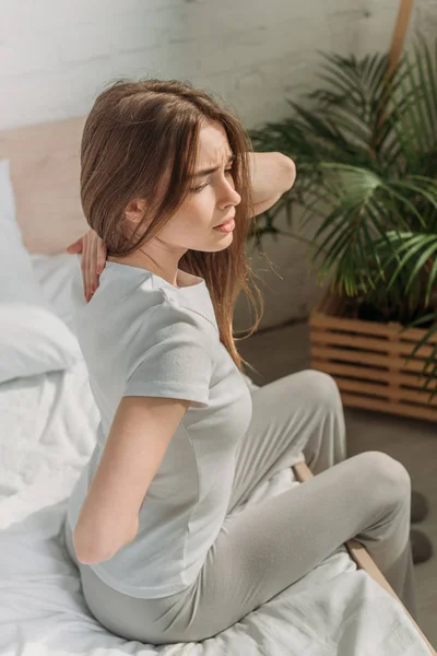 Giovane donna seduta sul letto e affetta da mal di schiena — Foto stock