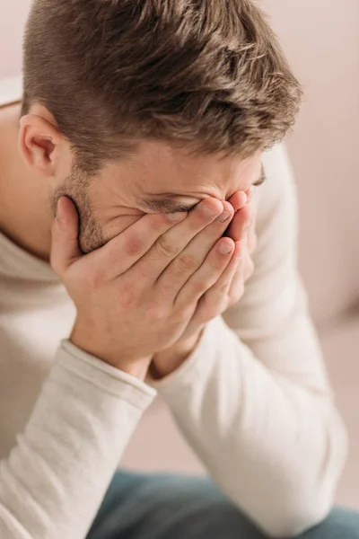 Молодой человек закрывает лицо руками, страдая от мигрени — стоковое фото
