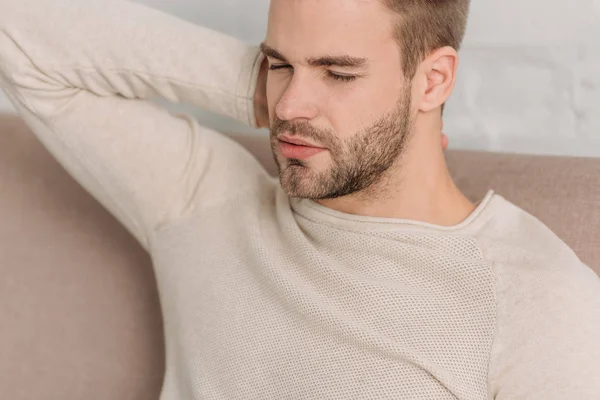 Mann mit geschlossenen Augen sitzt auf Sofa und leidet unter Nackenschmerzen — Stockfoto