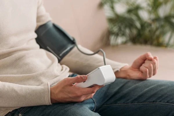 Abgeschnittene Ansicht eines Mannes, der zu Hause auf dem Sofa sitzt und Tonometer benutzt — Stockfoto