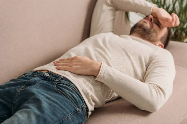 Selective focus of man lying on sofa and suffering from headache — Stock Photo