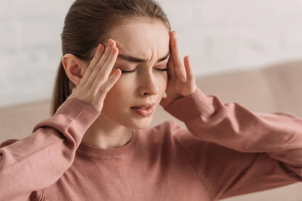 Jeune femme tenant la main près de la tête tout en souffrant de migraine avec les yeux fermés — Photo de stock