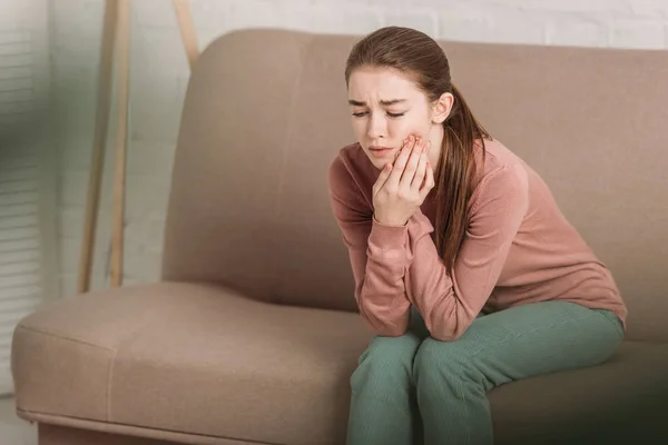 Несчастная девушка сидит на диване и страдает от зубной боли — стоковое фото
