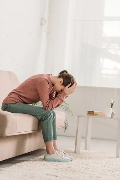 Femme malheureuse assise sur le canapé et souffrant de maux de tête — Photo de stock