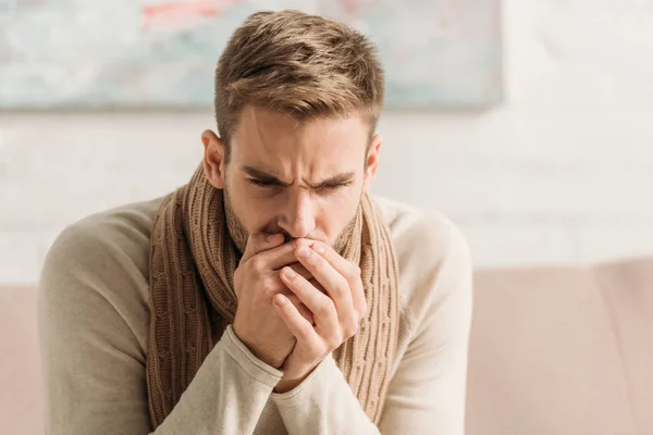 Diseased man in warm scarf coughing in folded hands — Stock Photo