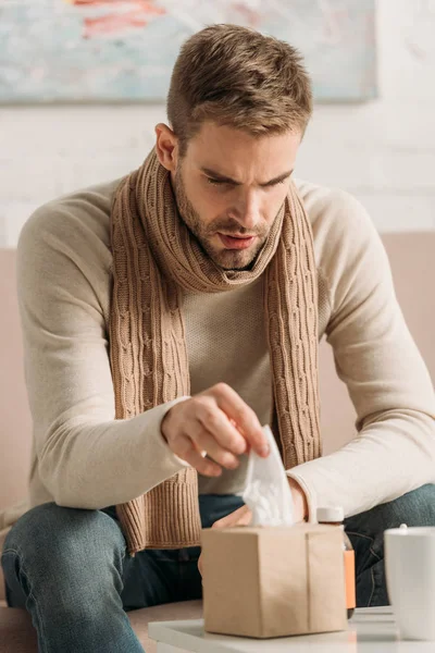 Diseased man in warm scarf taking napkin from pack — Stock Photo