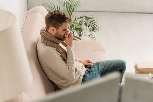 Selective focus of sick man sitting on sofa and sneezing in napkin — Stock Photo