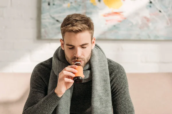 Хворий чоловік у теплому шарфі п'є сироп з закритими очима — стокове фото