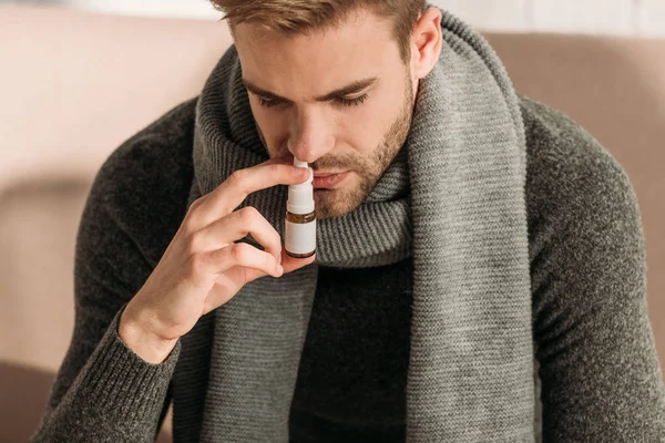Hombre enfermo en bufanda caliente y suéter usando aerosol nasal - foto de stock