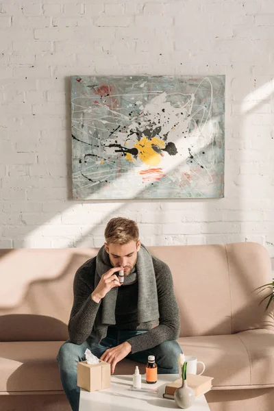 Kranker Mann sitzt mit Medikamenten auf Sofa neben Tisch und benutzt Nasenspray — Stockfoto