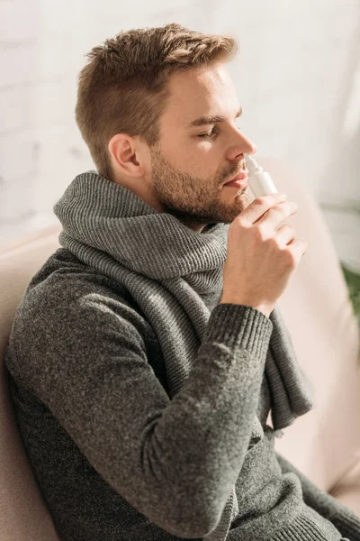 Uomo malato indossa sciarpa calda intorno al collo utilizzando spray nasale — Foto stock