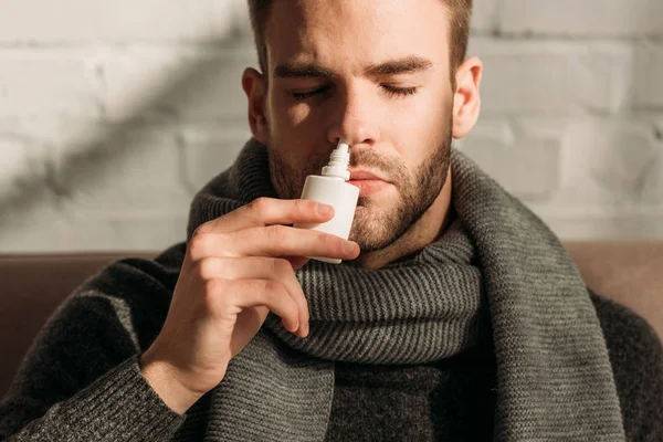 Sick young man sitting with closed eyes and using nasal spray — Stock Photo