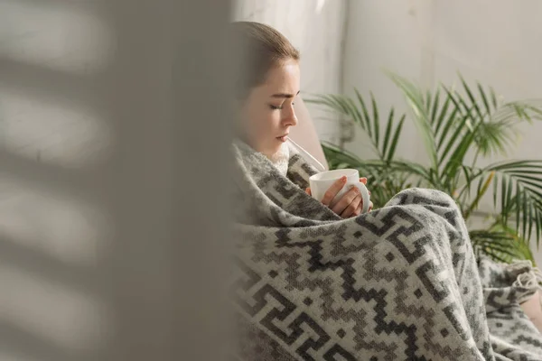 Selective focus of ill girl covered with blanket and holding cup of warming drink — Stock Photo