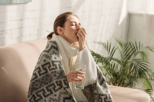 Menina doente, envolto em cobertor, segurando vidro de água e tomando remédio — Fotografia de Stock