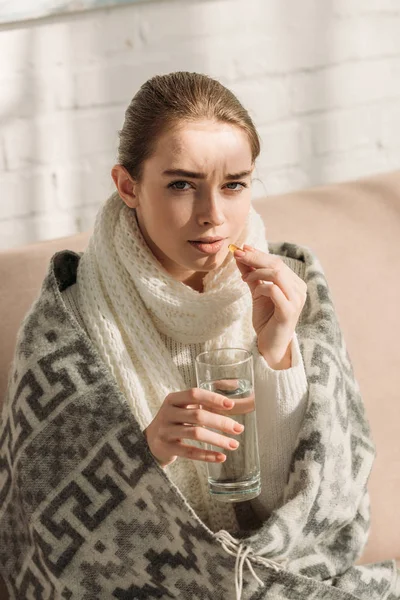 Krankes Mädchen blickt in Kamera, während es ein Glas Wasser hält und Medikamente nimmt — Stockfoto