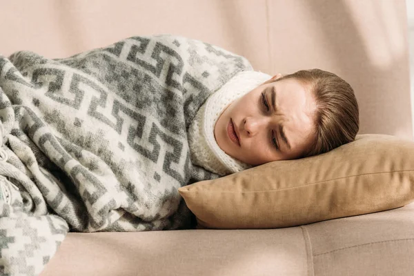 Хвора, засмучена дівчина лежить на дивані під ковдрою — стокове фото