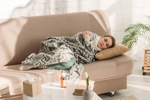 Femme malade couché sur le canapé sous couverture et regardant la caméra — Photo de stock