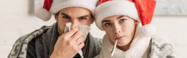 Colpo panoramico di coppia malata in cappelli di Babbo Natale guardando la fotocamera — Foto stock