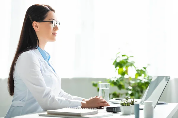 Schöne Ärztin sitzt mit Laptop in Klinik-Büro — Stockfoto
