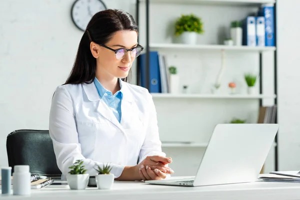 Médecin confiant ayant une consultation en ligne avec le patient sur ordinateur portable dans le bureau de la clinique — Photo de stock