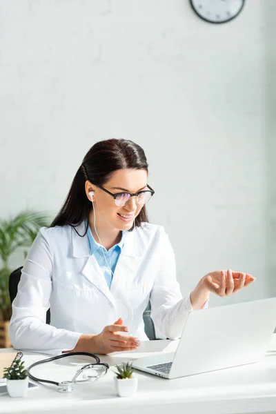 Hermoso médico que tiene consulta en línea con el paciente en el ordenador portátil en el consultorio clínico - foto de stock