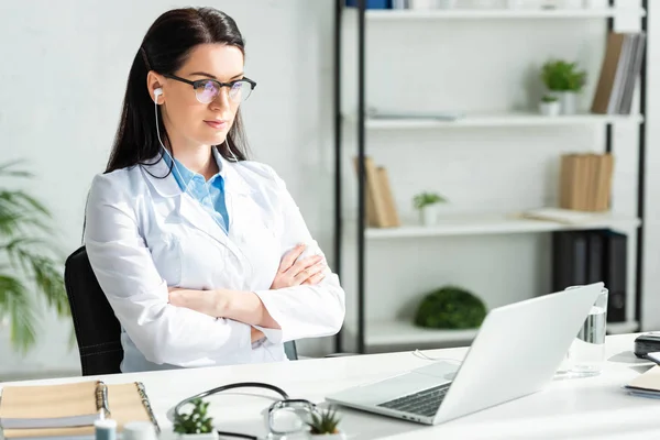 Female doctor with crossed arms having online consultation with patient on laptop in clinic office — Stock Photo